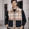 Man wearing Ashworth Wool Gilet in Oxley Check cream and brown tartan with navy contrast pockets over black long-sleeve top and dark trousers